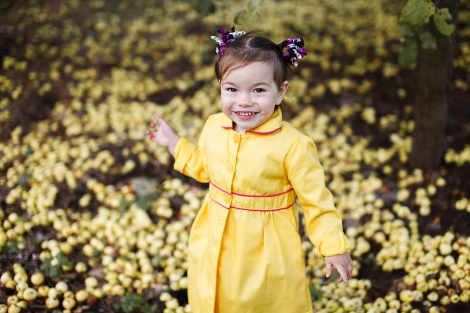 Фото девочки в желтом плаще среди желтых яблок